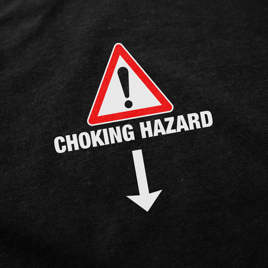 The Choking Hazard T-Shirt features a warning sign with an exclamation mark, the words "Choking Hazard," and a downward arrow on a black background, printed on ethically grown cotton.
