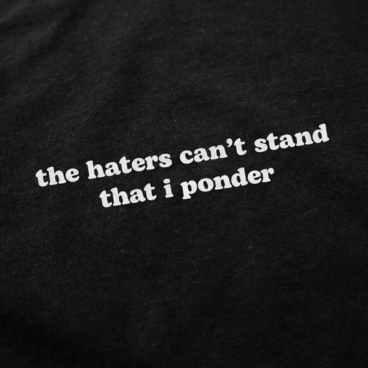 White text on black fabric reads "The Haters Can't Stand That I Ponder" in a bold, rounded font. This witty t-shirt is perfect for fans of clever, unique styles. Product: The Haters Can't Stand That I Ponder T-Shirt.