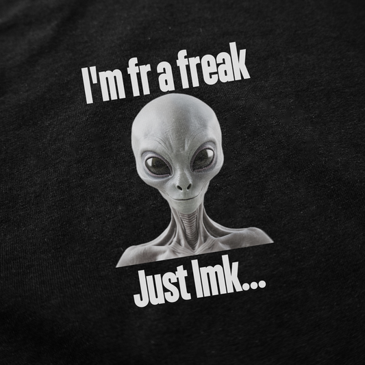 The I'm FR A Freak Just LMK... T-Shirt is 100% cotton and features a gray alien with large black eyes, white text reading "Im fr a freak" above and "Just lmk..." below, all on black. Part of the Illegal Shirts collection.