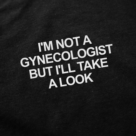 White text on black fabric reads: I'M NOT A GYNECOLOGIST BUT I'LL TAKE A LOOK—this "I'm Not a Gynecologist But I'll Take a Look T-Shirt" is a bold and funny conversation starter for any occasion.