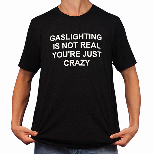 A person holds the sides of a Gaslighting Is Not Real You're Just Crazy T-Shirt, featuring the bold white phrase "GASLIGHTING IS NOT REAL YOURE JUST CRAZY"—perfect for fans of edgy and Illegal Shirts humor.