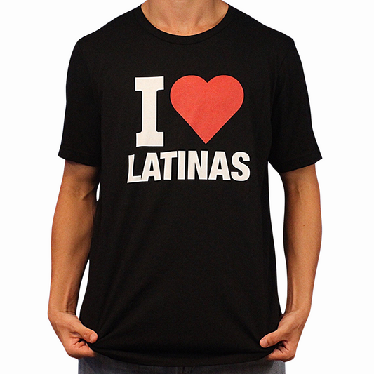 Wearing the I Heart Latinas T-Shirt, a person poses holding the sides of this black tee, which features bold white and red "I ♥ LATINAS" text across the front. It’s made from ethically grown cotton.