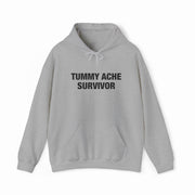 The Tummy Ache Survivor Hoodie is a light gray cotton-polyester sweatshirt with a front pocket, drawstrings, and bold black "TUMMY ACHE SURVIVOR" text—perfect for Illegal Shirts fans.