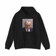 The Trump Mug Shot Hoodie is a black hoodie featuring a printed photo of a blond man in a suit and tie with a serious expression, and includes a tear-away label for added comfort.