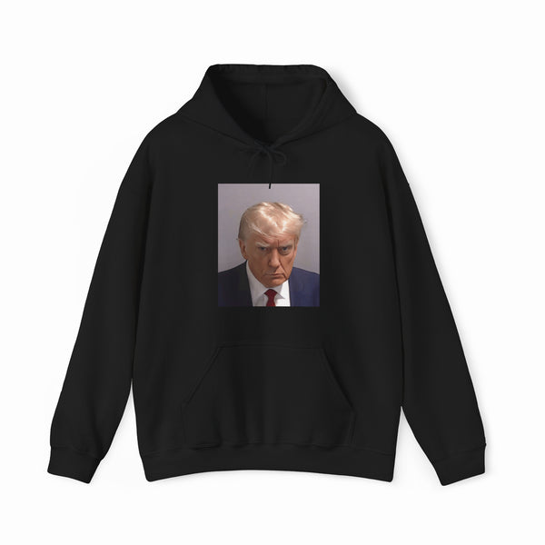 The Trump Mug Shot Hoodie is a black hoodie featuring a printed photo of a blond man in a suit and tie with a serious expression, and includes a tear-away label for added comfort.