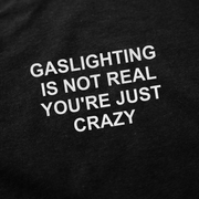 The Gaslighting Is Not Real You're Just Crazy T-Shirt features bold white text on black fabric that reads: “Gaslighting is not real you’re just crazy.”.