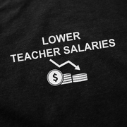 Featuring a black background with 'LOWER TEACHER SALARIES' above a downward arrow pointing to coins and a dollar sign, the Lower Teacher Salaries T-Shirt is a bold, funny shirt designed to spark conversation.
