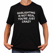 A person holds the sides of a Gaslighting Is Not Real You're Just Crazy T-Shirt, featuring the bold white phrase "GASLIGHTING IS NOT REAL YOURE JUST CRAZY"—perfect for fans of edgy and Illegal Shirts humor.