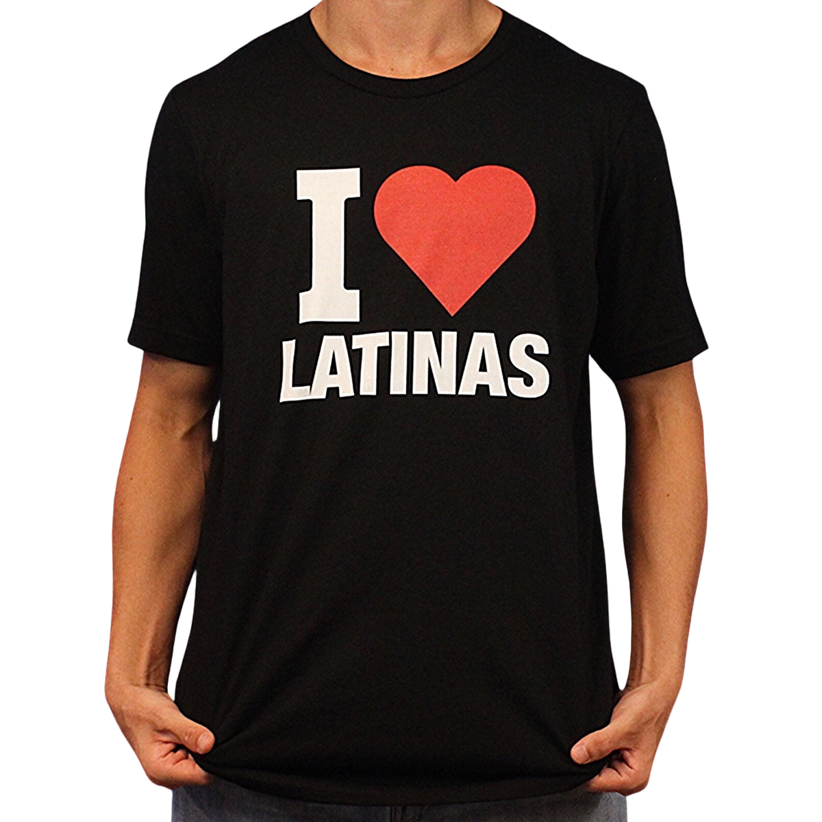 Wearing the I Heart Latinas T-Shirt, a person poses holding the sides of this black tee, which features bold white and red "I ♥ LATINAS" text across the front. It’s made from ethically grown cotton.