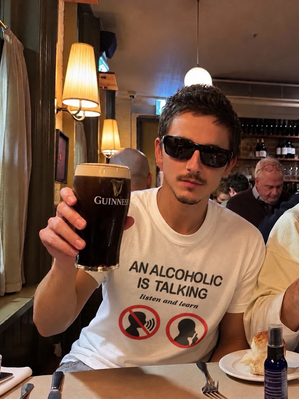 A person at a pub wearing the An Alcoholic Is Talking Listen And Learn T-Shirt