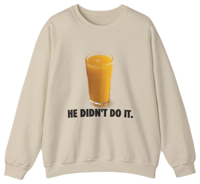 The He Didn't Do It Crewneck is a beige sweatshirt with a glass of orange juice above bold black text—ideal for fans of funny shirts or anyone seeking unique Illegal Shirts with a playful twist.